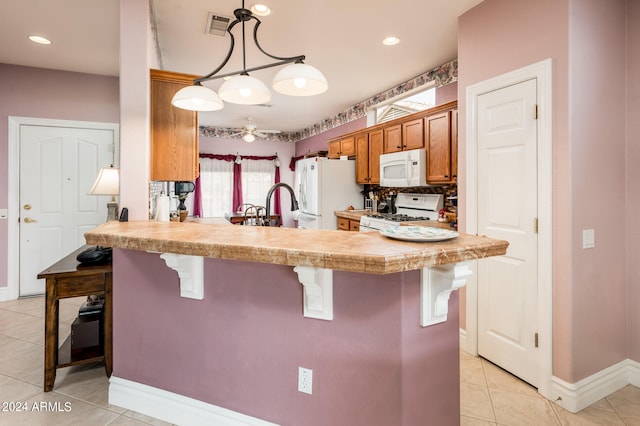 kitchen featuring pendant lighting, white appliances, a notable chandelier, a kitchen bar, and light tile floors