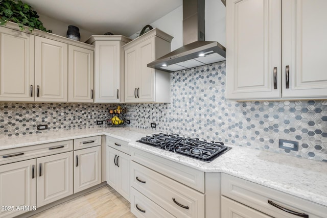 kitchen featuring wall chimney range hood, black gas cooktop, tasteful backsplash, and light stone counters