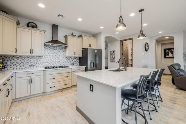 kitchen featuring arched walkways, stainless steel fridge, gas stovetop, and wall chimney range hood