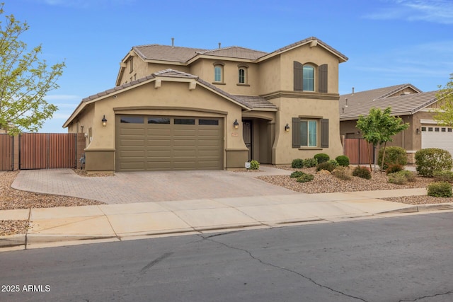 mediterranean / spanish home with decorative driveway, a tile roof, stucco siding, and fence