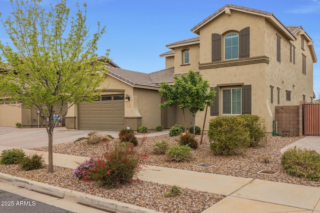 mediterranean / spanish house with fence, a tiled roof, concrete driveway, stucco siding, and a garage