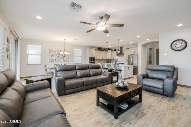 living room with visible vents, ceiling fan with notable chandelier, recessed lighting, light wood-style floors, and arched walkways