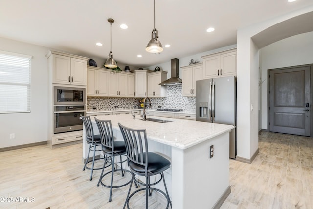 kitchen featuring a sink, decorative backsplash, appliances with stainless steel finishes, and wall chimney exhaust hood