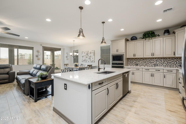 kitchen featuring visible vents, an island with sink, stainless steel appliances, a sink, and open floor plan