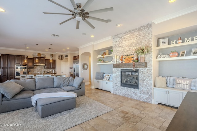 living room with a fireplace, built in features, ceiling fan, and ornamental molding