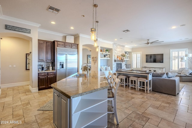 kitchen with a kitchen breakfast bar, ceiling fan, a kitchen island with sink, sink, and built in fridge