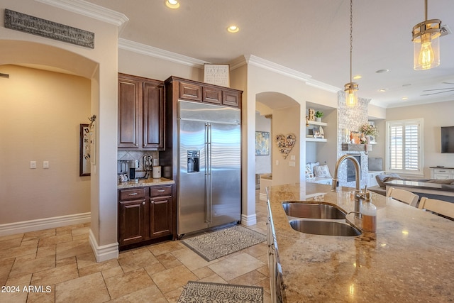 kitchen featuring light stone countertops, ornamental molding, sink, built in refrigerator, and hanging light fixtures