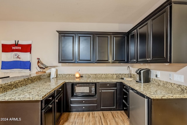 kitchen with light stone counters, black microwave, sink, light hardwood / wood-style flooring, and stainless steel refrigerator