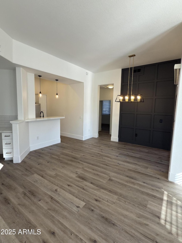 unfurnished living room with a sink, a textured ceiling, baseboards, and wood finished floors