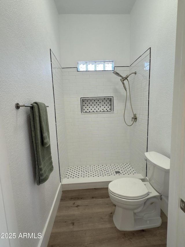 full bath featuring a tile shower, wood finished floors, and toilet