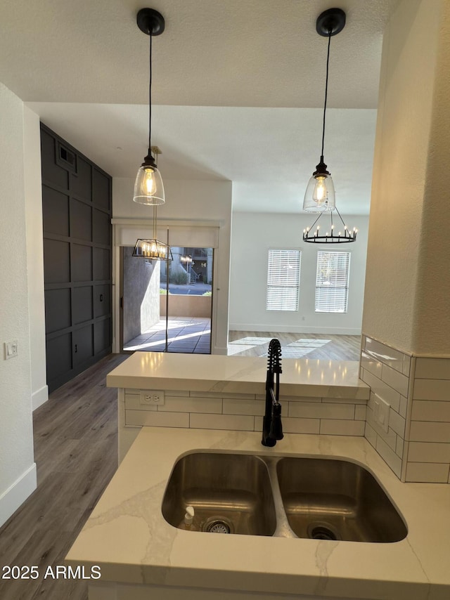 kitchen with light stone countertops, decorative light fixtures, a sink, and wood finished floors