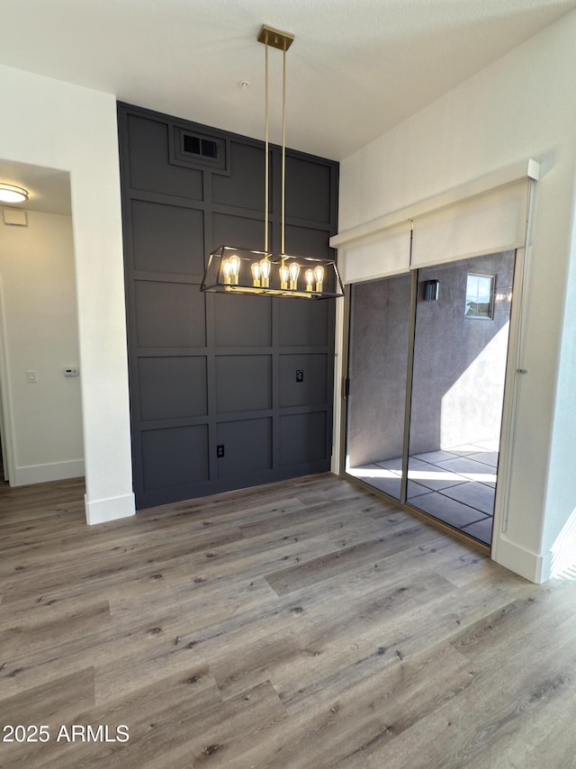 unfurnished dining area featuring baseboards, wood finished floors, visible vents, and a decorative wall