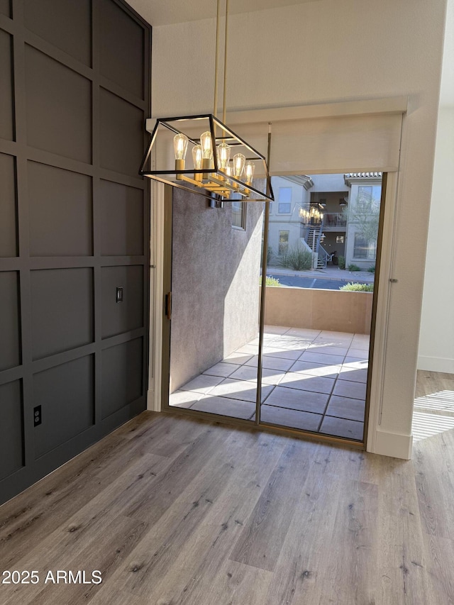 unfurnished dining area with a notable chandelier, a decorative wall, and wood finished floors