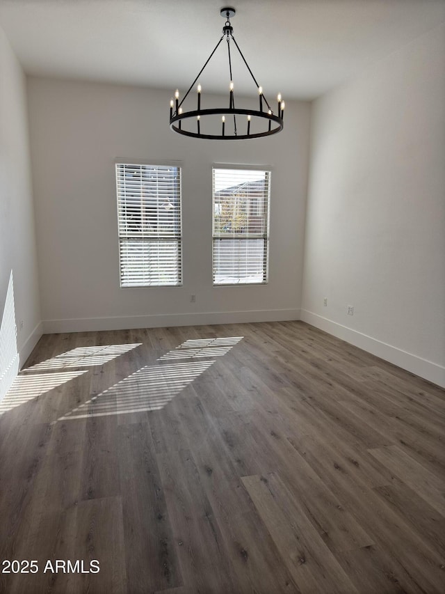 unfurnished dining area featuring a chandelier, baseboards, and wood finished floors