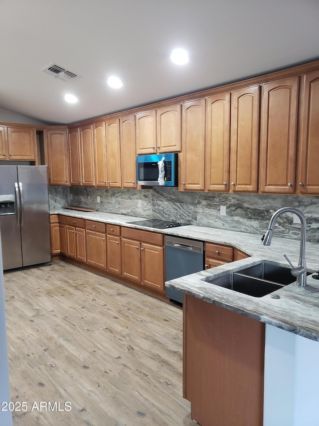 kitchen with light stone countertops, appliances with stainless steel finishes, tasteful backsplash, sink, and light hardwood / wood-style flooring