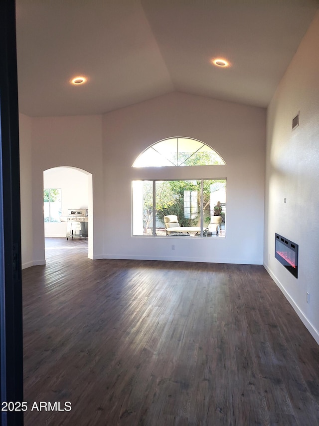 unfurnished living room with dark wood-type flooring, heating unit, lofted ceiling, and a healthy amount of sunlight