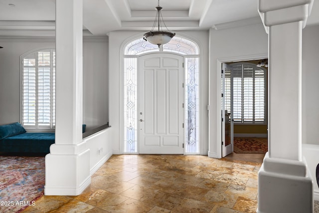 foyer entrance with ornate columns, stone finish flooring, baseboards, and a raised ceiling