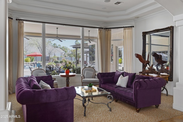 carpeted living area with baseboards, ornamental molding, visible vents, and a ceiling fan