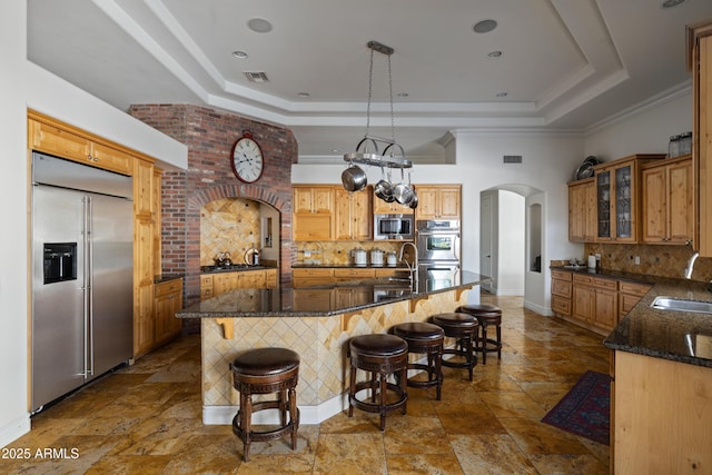 kitchen featuring built in appliances, a tray ceiling, arched walkways, and a sink