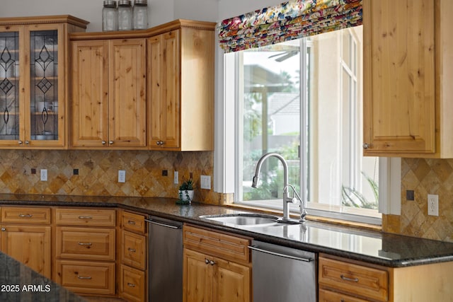 kitchen featuring tasteful backsplash, dark stone counters, glass insert cabinets, a sink, and stainless steel dishwasher