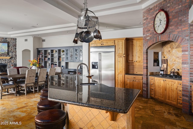 kitchen featuring arched walkways, a sink, a kitchen breakfast bar, a tray ceiling, and stainless steel built in refrigerator