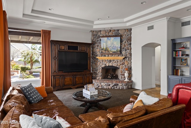 living area with visible vents, arched walkways, a tray ceiling, and a stone fireplace