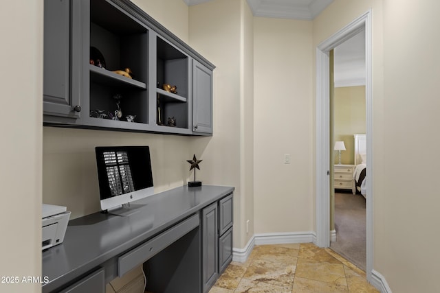 office space featuring stone finish flooring, baseboards, built in desk, and ornamental molding