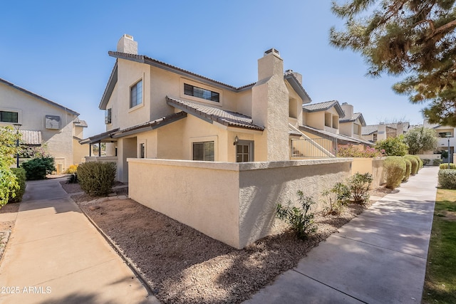 view of home's exterior featuring a tile roof, a fenced front yard, a chimney, and stucco siding