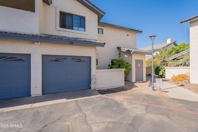 view of front of home featuring an attached garage, driveway, a tiled roof, and stucco siding