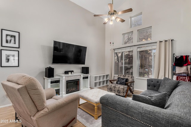 living area featuring a towering ceiling, baseboards, a ceiling fan, and wood finished floors