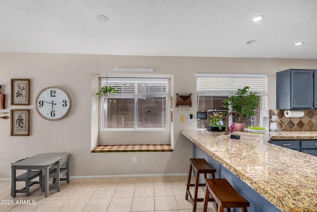 kitchen featuring a sink, blue cabinetry, a kitchen breakfast bar, light tile patterned floors, and decorative backsplash