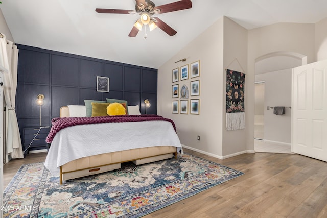 bedroom featuring a ceiling fan, wood finished floors, baseboards, lofted ceiling, and a decorative wall