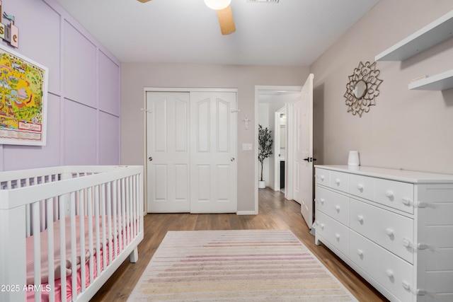 bedroom with a closet, a ceiling fan, a nursery area, and wood finished floors