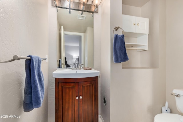 half bathroom featuring visible vents, toilet, and vanity