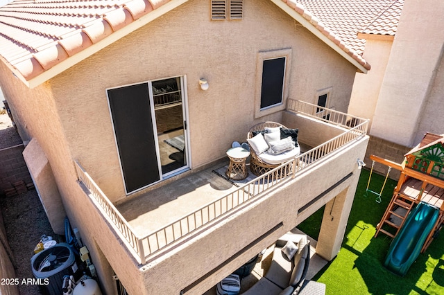 exterior space with a balcony, a tiled roof, a playground, and stucco siding