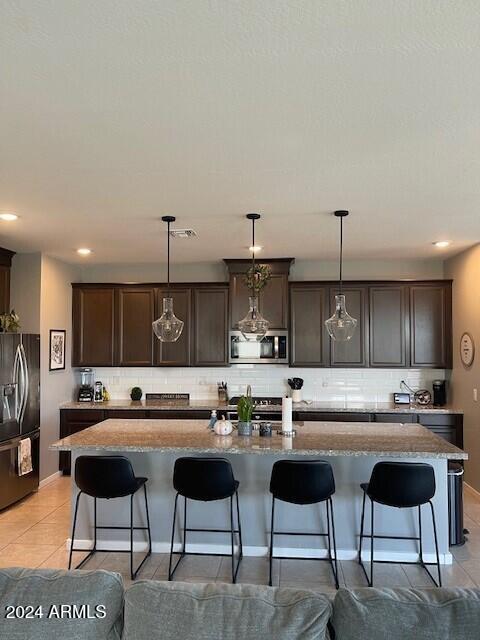 kitchen with dark brown cabinets, black fridge, hanging light fixtures, and an island with sink