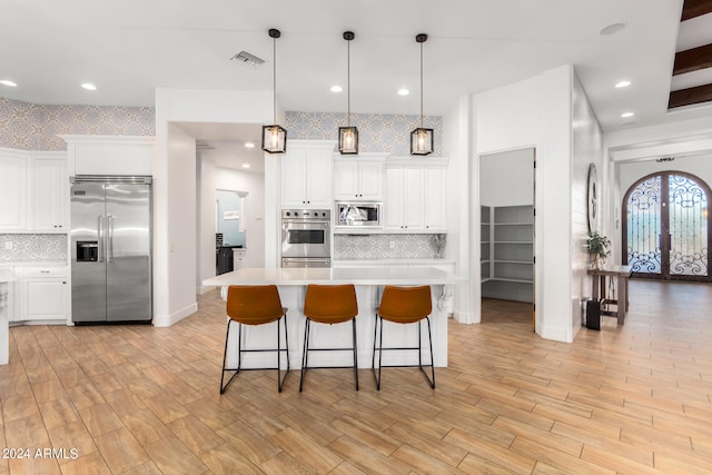 kitchen with built in appliances, decorative light fixtures, light hardwood / wood-style floors, and white cabinets