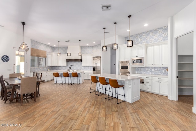 kitchen with white cabinetry, hanging light fixtures, a large island with sink, built in appliances, and light hardwood / wood-style floors