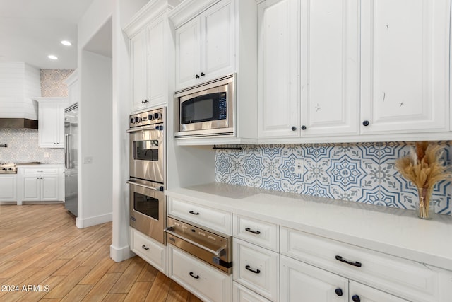 kitchen with tasteful backsplash, built in appliances, white cabinetry, and light hardwood / wood-style flooring