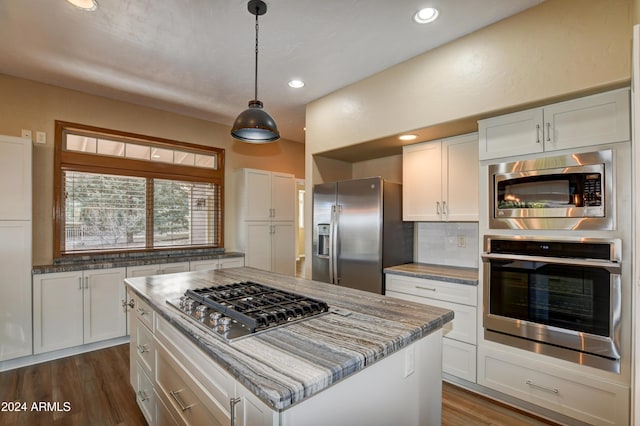 kitchen featuring decorative backsplash, stainless steel appliances, dark wood-type flooring, white cabinets, and a kitchen island