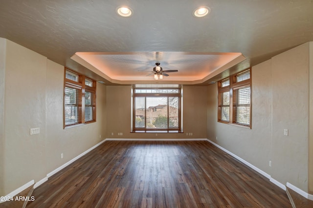 empty room with a textured ceiling, a tray ceiling, ceiling fan, and dark wood-type flooring