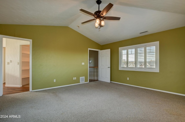 unfurnished bedroom with a walk in closet, ceiling fan, carpet floors, and lofted ceiling