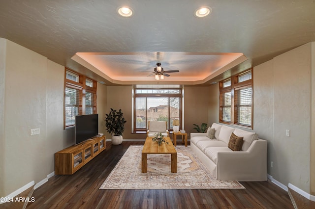 living room featuring a tray ceiling, ceiling fan, dark hardwood / wood-style flooring, and a textured ceiling