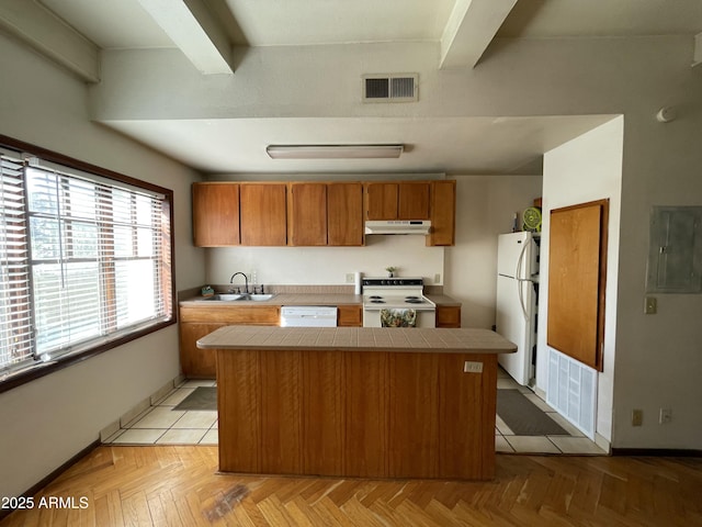 kitchen with under cabinet range hood, white appliances, a sink, visible vents, and tile counters