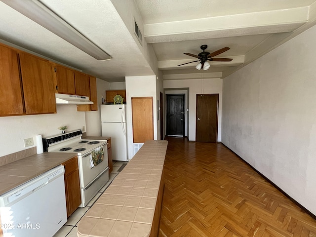 kitchen with brown cabinets, tile counters, visible vents, white appliances, and under cabinet range hood