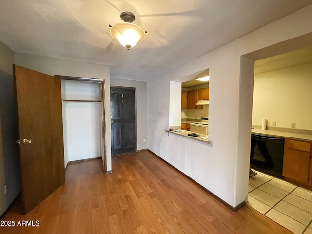 interior space with black dishwasher, brown cabinetry, stove, light countertops, and light wood-type flooring