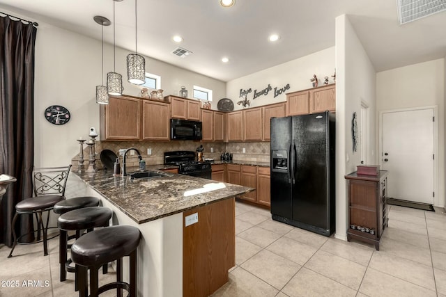 kitchen with kitchen peninsula, a breakfast bar area, dark stone counters, hanging light fixtures, and black appliances