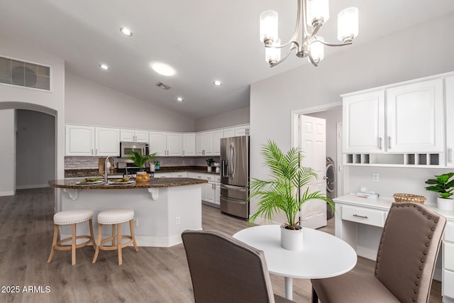 kitchen with a center island with sink, visible vents, white cabinets, arched walkways, and stainless steel appliances