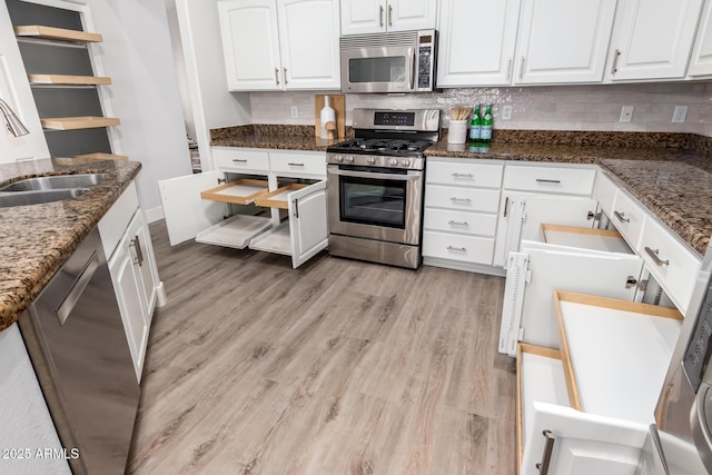 kitchen featuring white cabinets, decorative backsplash, dark stone counters, appliances with stainless steel finishes, and light wood-style floors