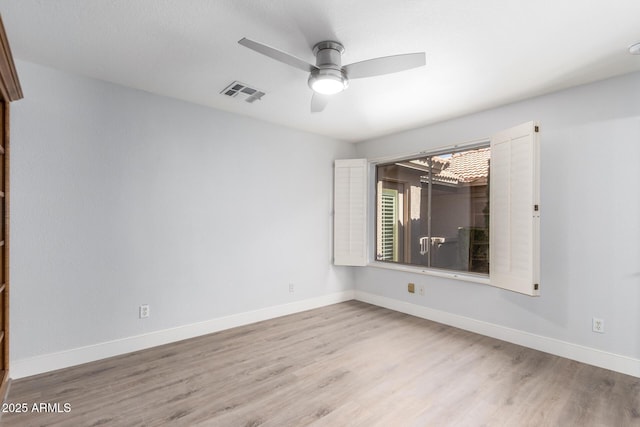 spare room with light wood-style floors, a ceiling fan, visible vents, and baseboards